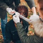 Guys help a woman. African girl sitting unconscious. Providing first aid in the park